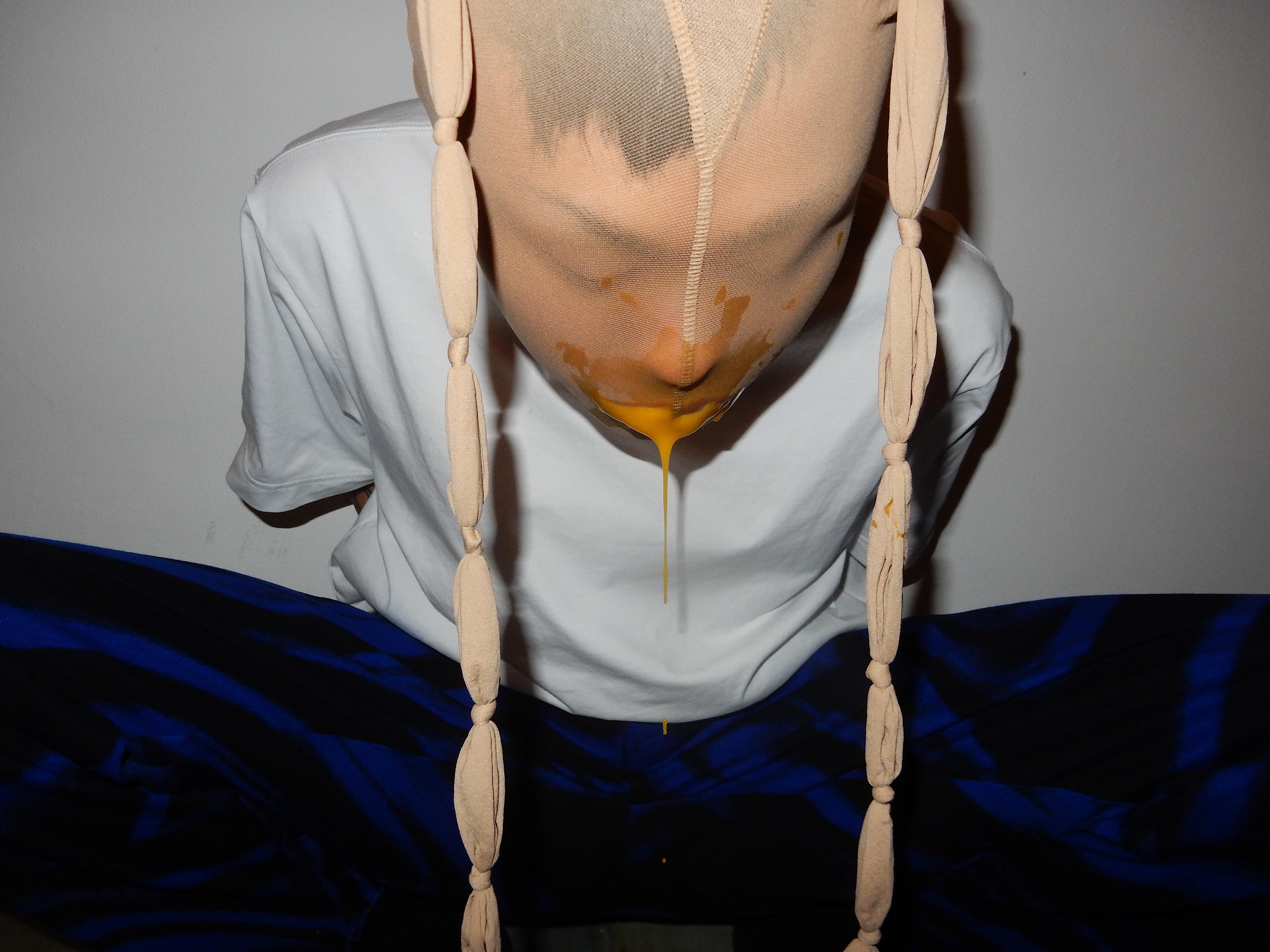 Person vomiting an orange liquid, with flesh-colored tights on the head, from Funkenstein