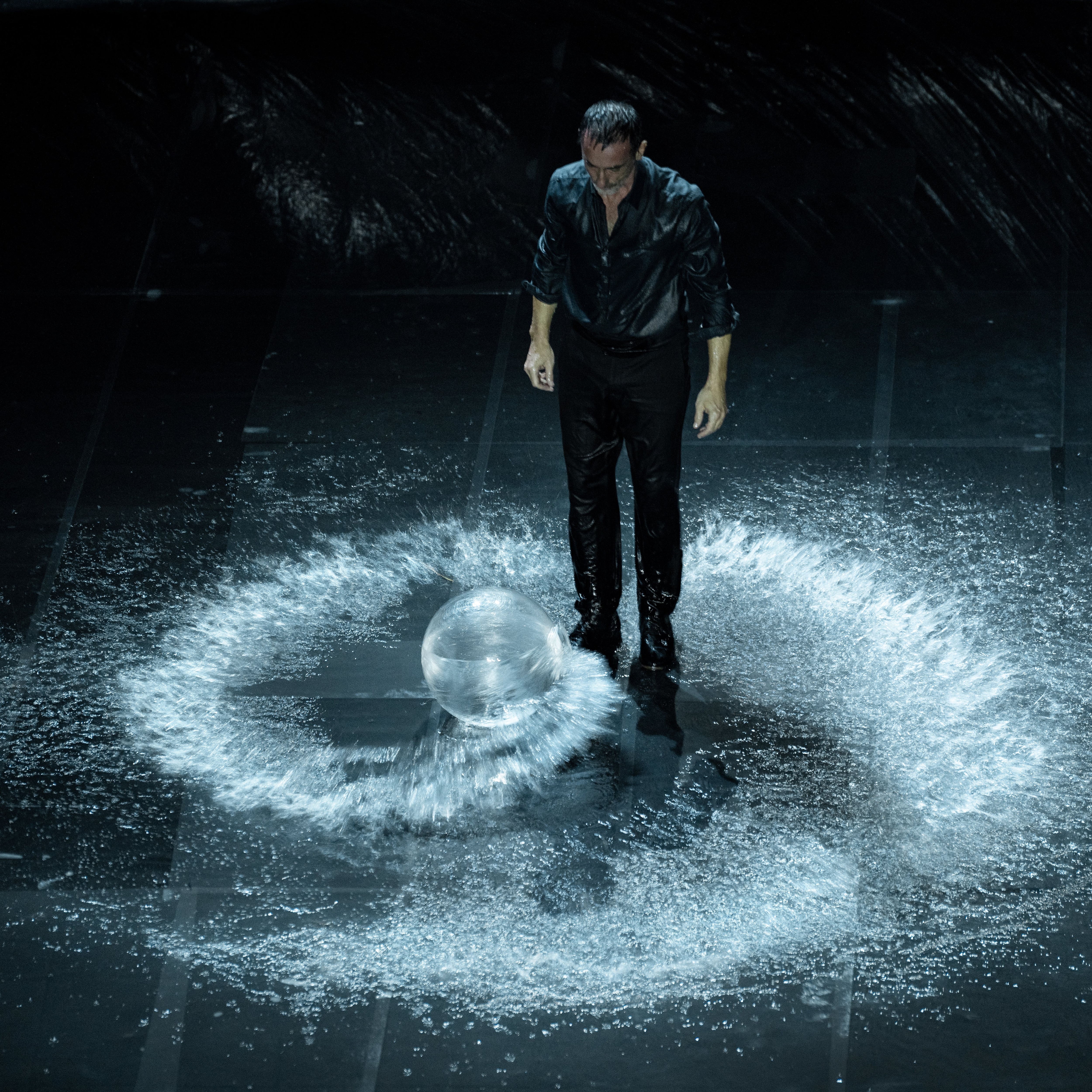 照片：男人独自站在水漩涡中，面向一个透明的球体。